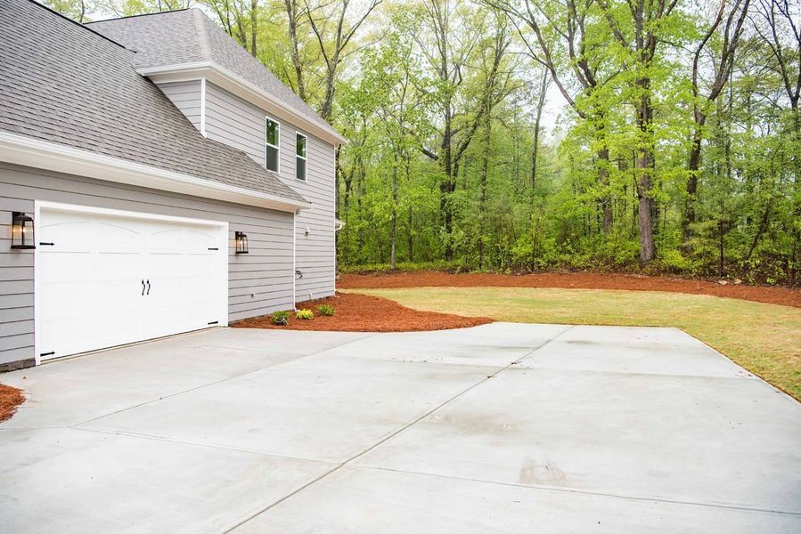 Garage with a concrete driveway and a wooded backdrop.