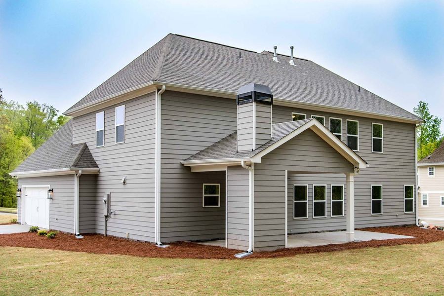Gray two-story house with a garage, chimney, and covered patio on a grassy lawn under a blue sky.