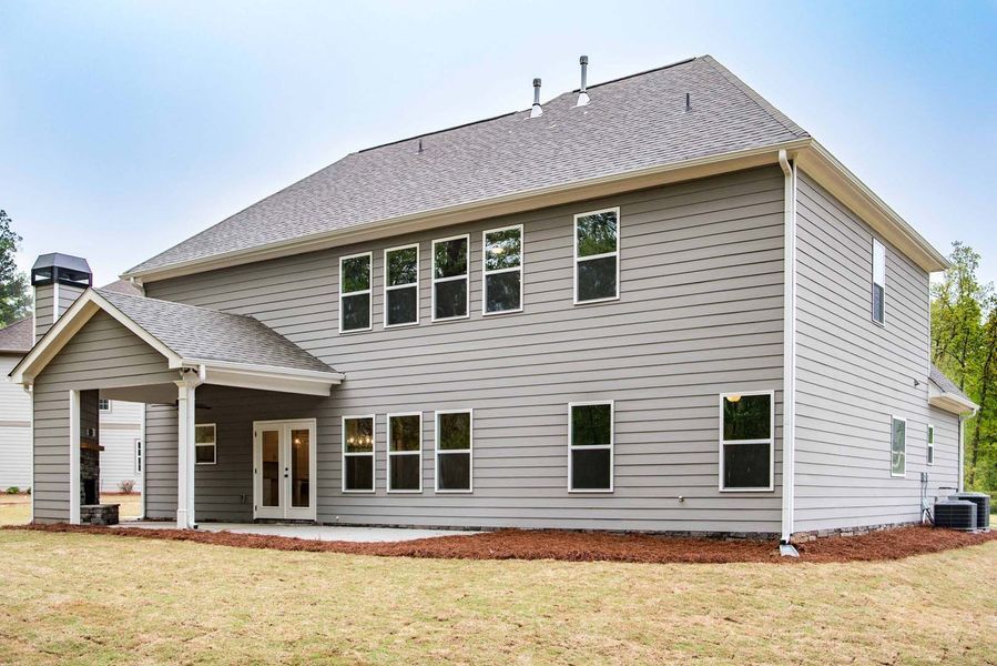 Back of a gray two-story house with multiple windows, a patio, and a small covered porch under a cloudy sky.