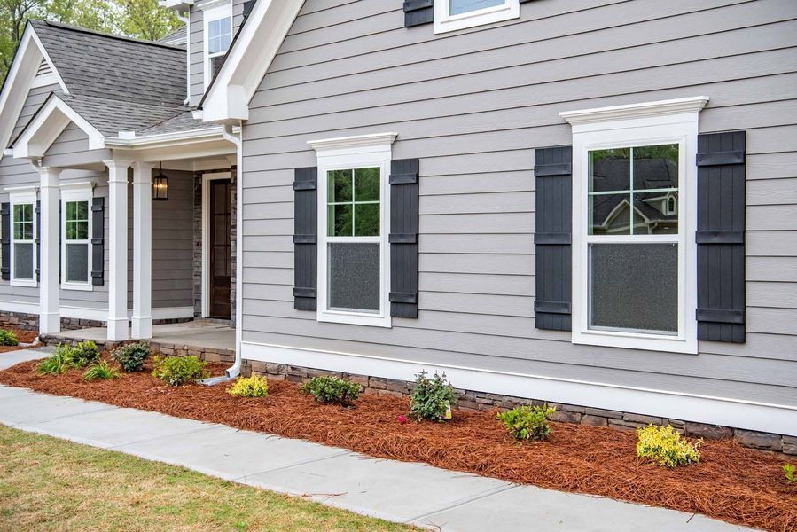 Gray house with white trim, black shutters, and landscaping.