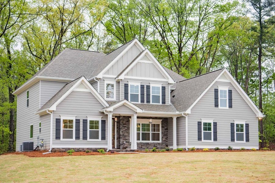 Gray two-story house with dark shutters, a stone entry, and a grassy yard in front of trees.