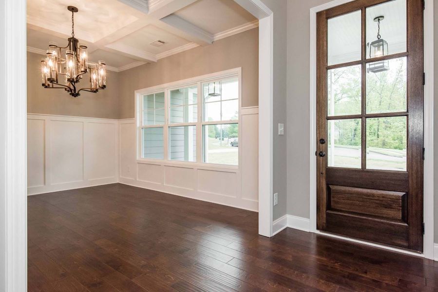 Dining room with dark wood floors, chandelier, white wainscoting, and a brown door with glass panels.