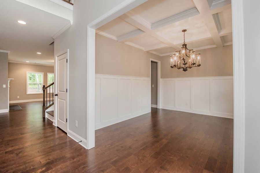 Empty dining room with wood floors, white wainscoting, and a chandelier, viewed from the hallway.