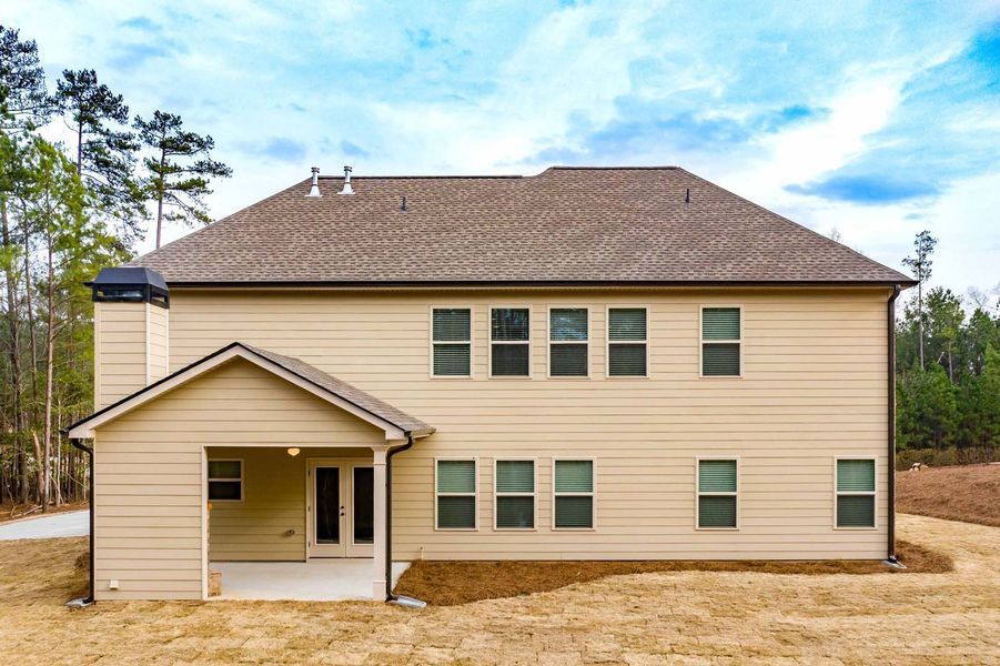 Rear view of a two-story tan house with a porch, brown roof, and chimney, against a blue sky.