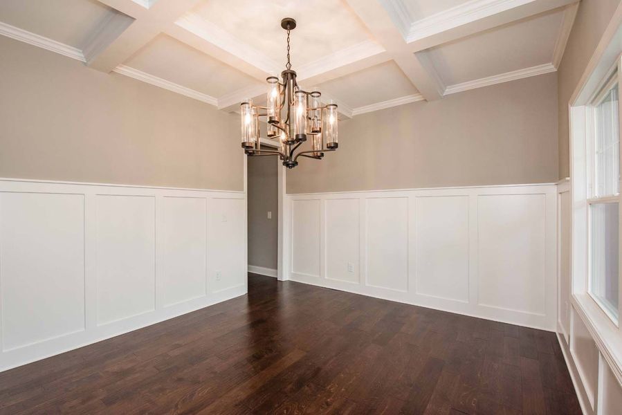 Empty dining room with dark wood floor, wainscoting, beige walls, and chandelier.