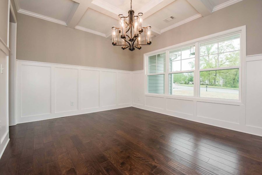 Empty dining room with dark wood floor, white wainscoting, tan walls, and chandelier.