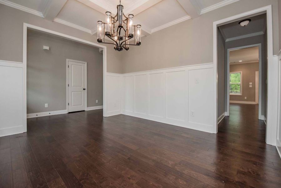 Empty dining room with dark wood floors, white wainscoting, grey walls, chandelier, and door.