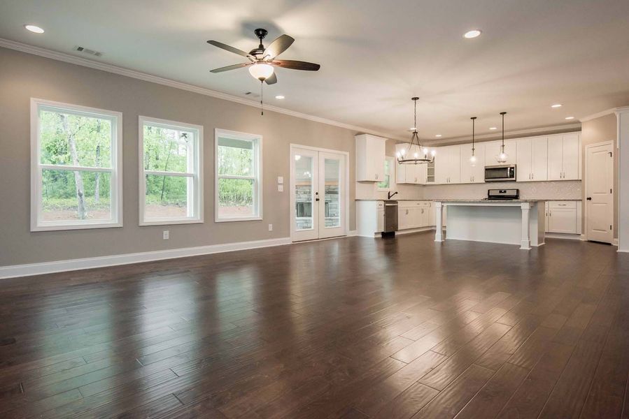 Open-concept living space with hardwood floors, white kitchen, and gray walls. Three windows and French doors let in light.