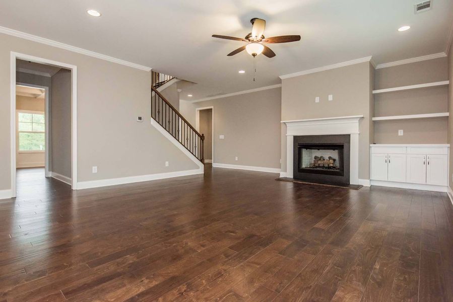 Empty living room with dark wood floors, fireplace, and built-in shelving.