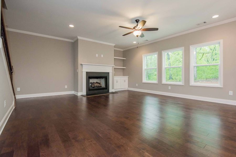 Empty living room with dark wood floors, fireplace, and windows.