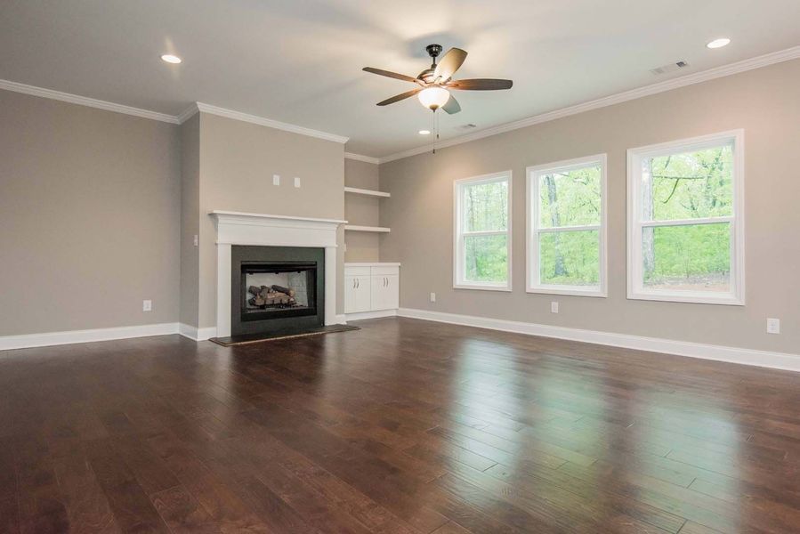 Empty living room with fireplace, windows, and hardwood floors.