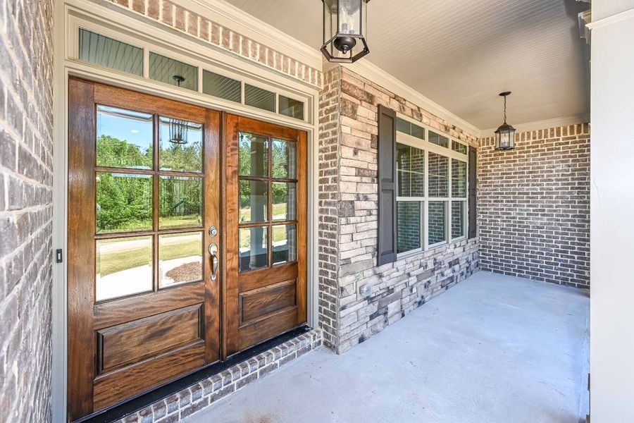 Brown double doors with glass panes on a brick porch, two hanging lights, a window with shutters.