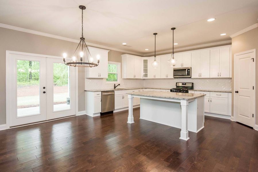 Open kitchen with white cabinets, island, and dark wood floors. Includes a chandelier and doors.