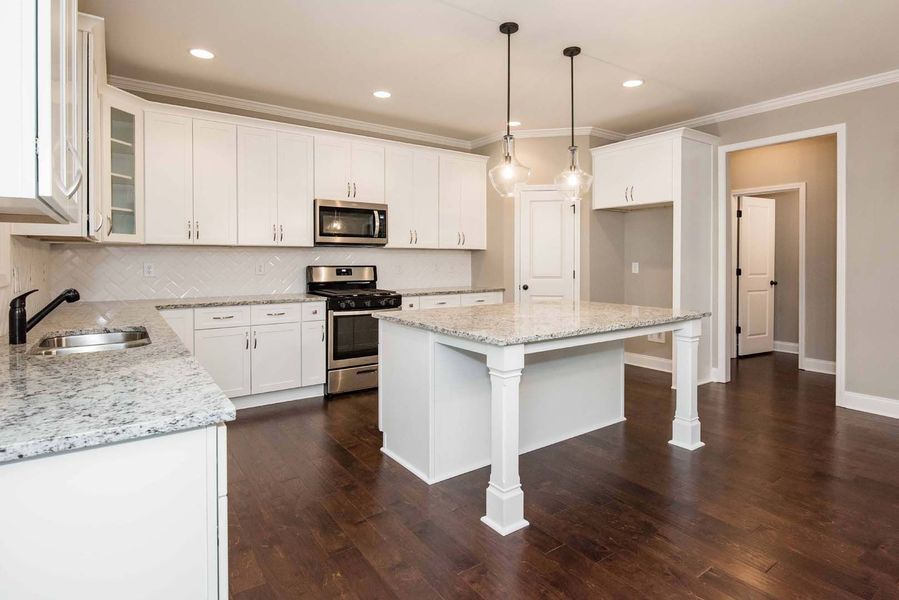 White kitchen with island, granite counters, dark wood floors, stainless steel appliances.