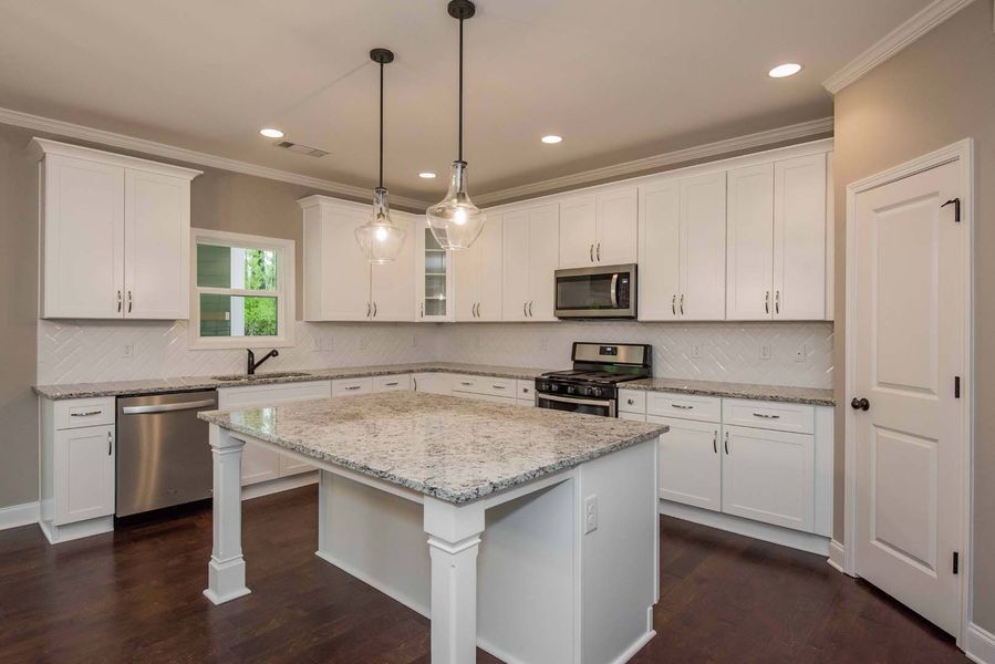 White kitchen with granite countertops, island, and dark wood floors.