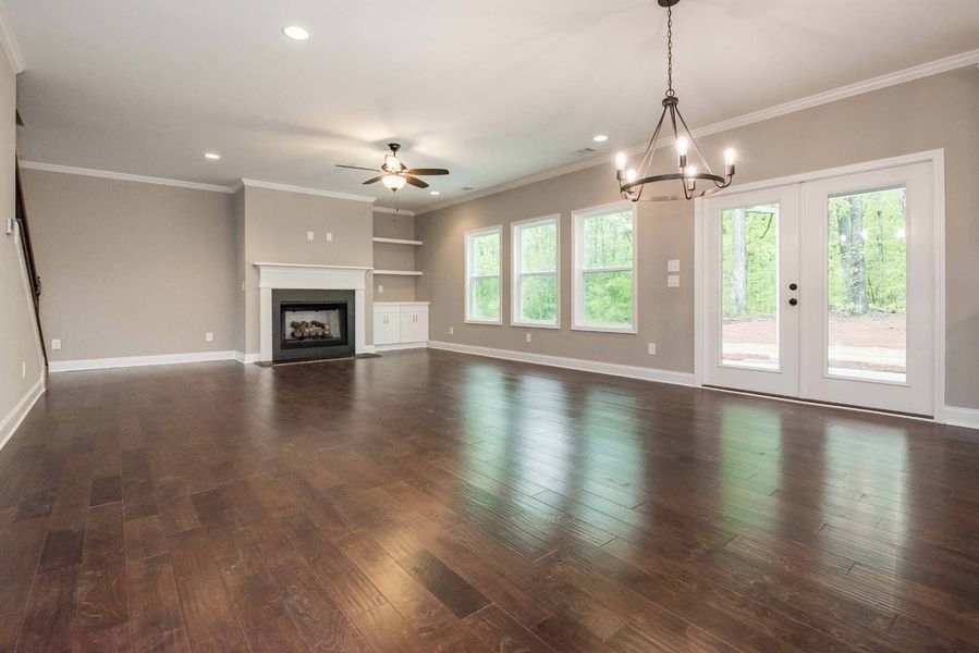 Empty living room with hardwood floors, fireplace, windows, and French doors.
