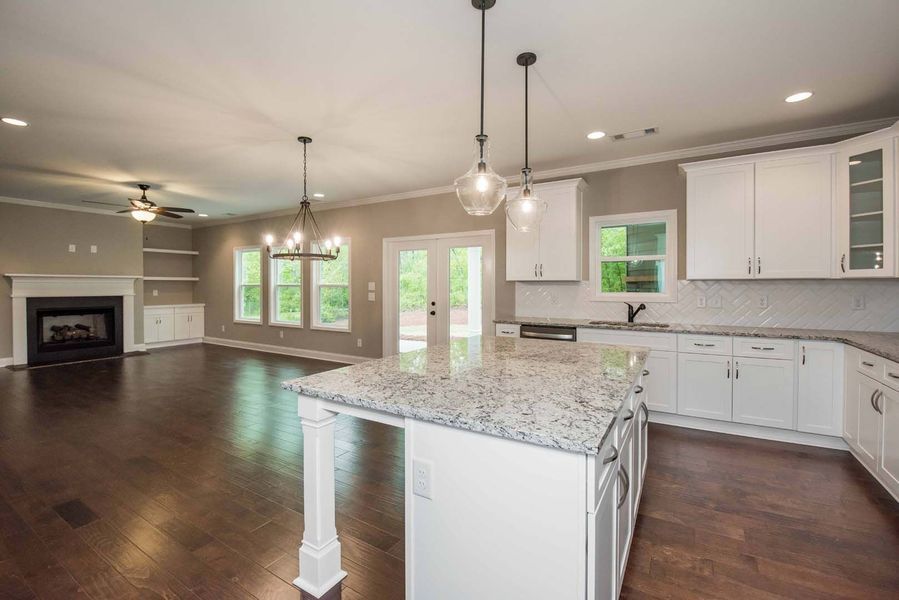 Spacious kitchen with white cabinets, granite countertops, island, and hardwood floors. Opens to living area with fireplace.