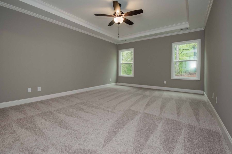Empty bedroom with gray walls, light carpet, two windows, and ceiling fan.