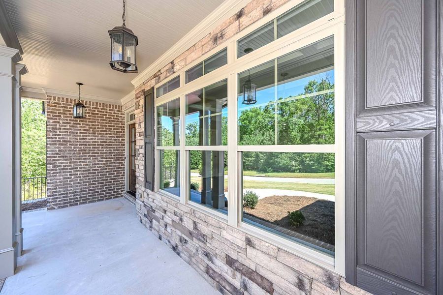 Covered porch with brick and stone walls, large windows, gray shutters, and hanging lights.