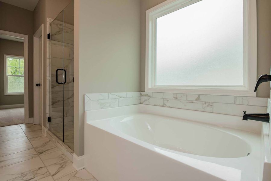 Bathroom with white tub, marble tile, frosted window, and glass shower.