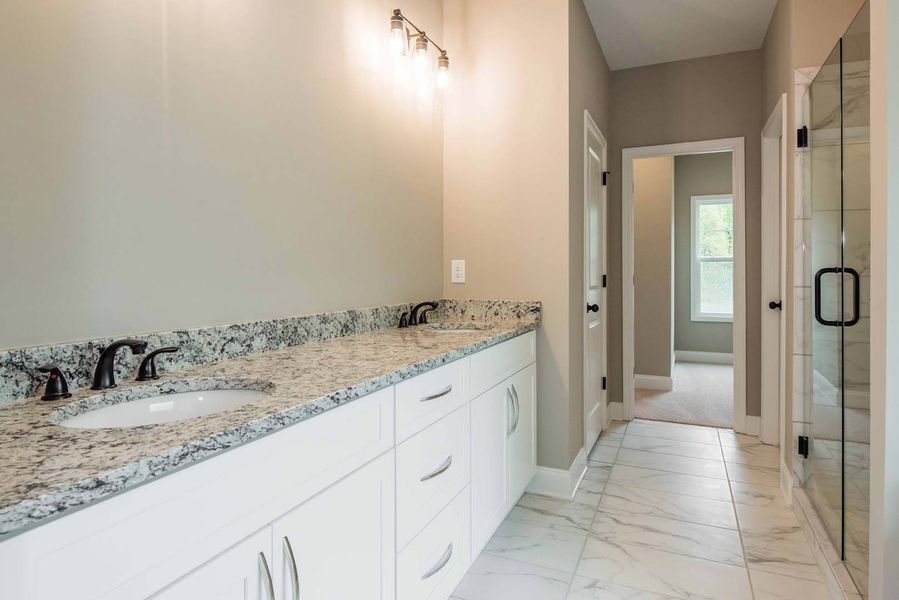 Bathroom with white cabinets, granite countertop, marble floor, and a glass shower.