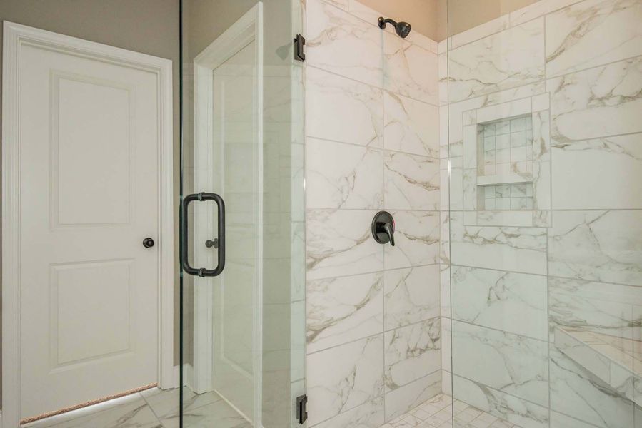 Bathroom with marble tiled shower, glass door, and white door on the left.