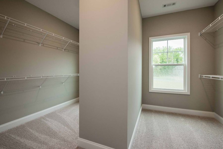 Walk-in closet with neutral walls, wire shelving, and a window; light-colored carpet.