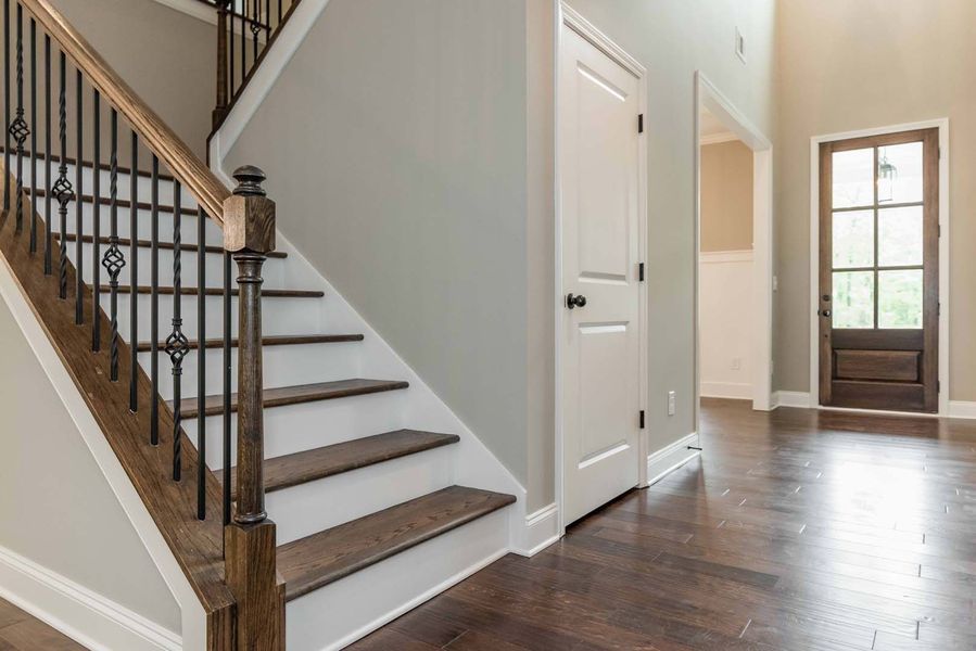 Wooden staircase with wrought iron railing, white door, and dark wood front door.