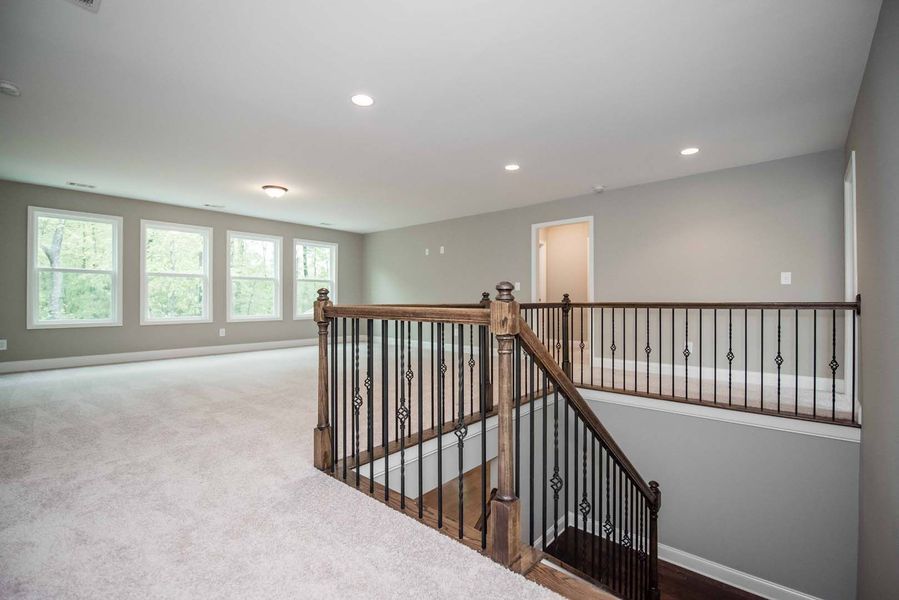 Open room with staircase and railing, gray walls, carpet, and windows.