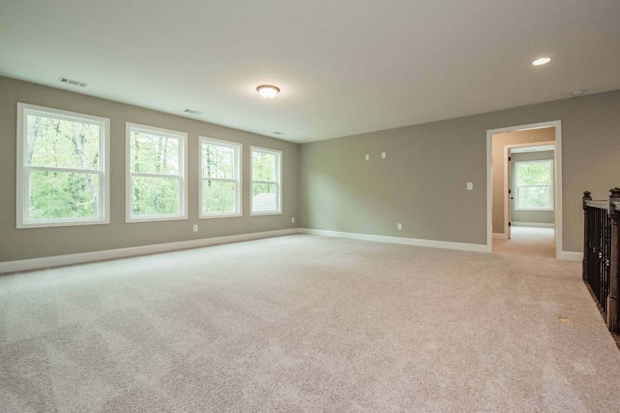 Spacious room with neutral walls, carpet, and large windows. A doorway leads to an open space.