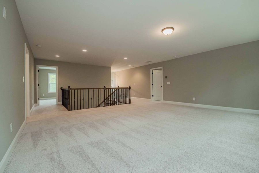Spacious, carpeted room with gray walls, stairs, and multiple doors.