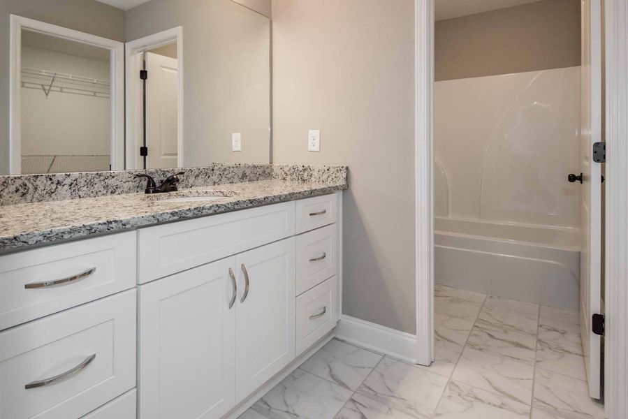 White bathroom with marble vanity, tub, and tiled floor.