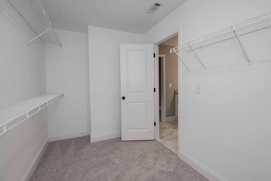 Empty white walk-in closet with wire shelves and a door leading to a bathroom.