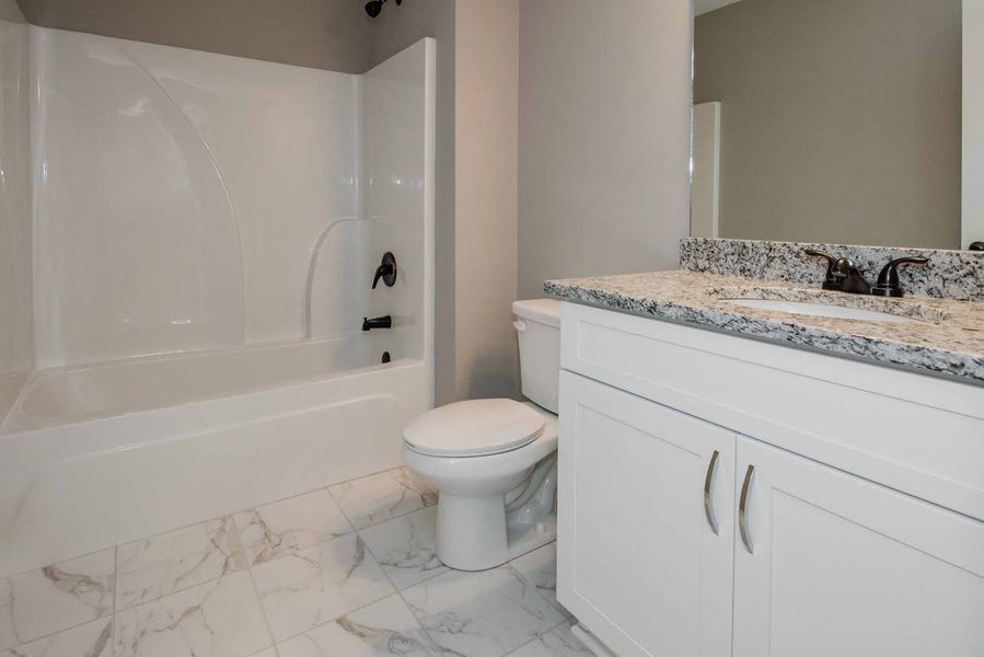 A bathroom with a white tub, toilet, vanity, and marble floor. Black fixtures and gray walls.