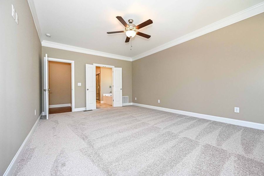 Empty bedroom with beige walls, carpet, and a ceiling fan. Two doorways lead to other rooms.