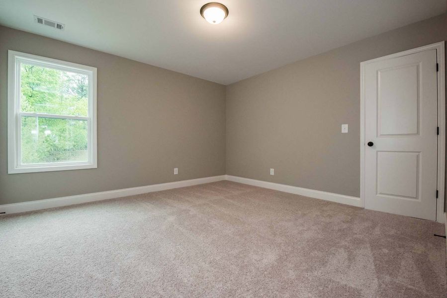 Empty bedroom with beige walls, light-colored carpet, white trim, window, and door.