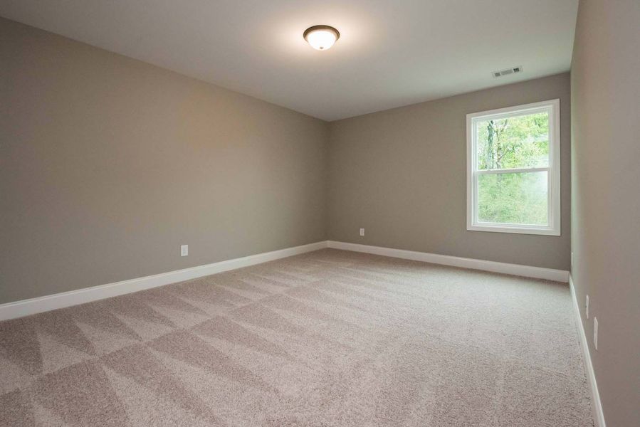 Empty bedroom with beige walls, patterned carpet, and a window.