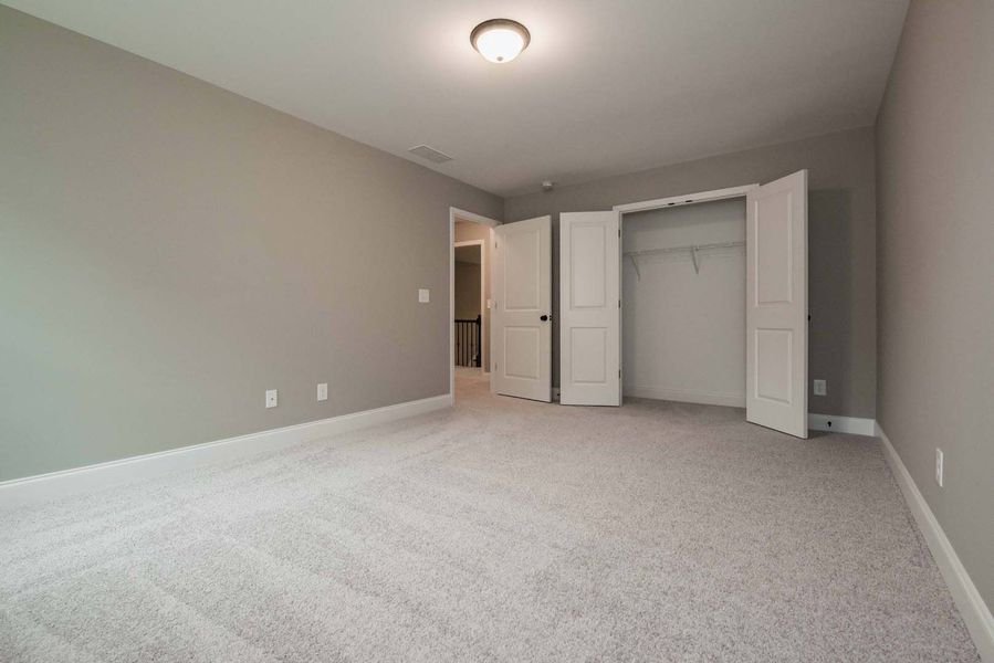Empty bedroom with gray walls, carpet, open closet, and a doorway.