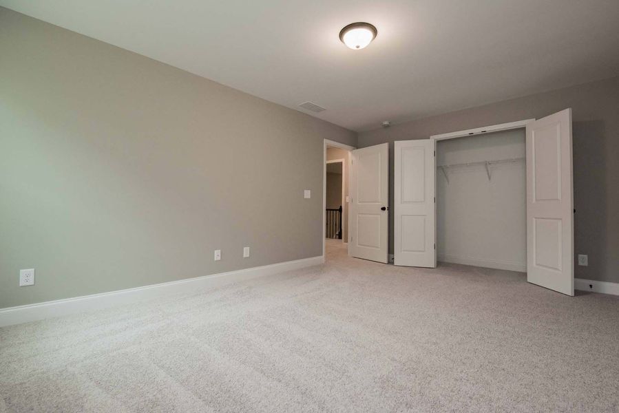 Empty bedroom with gray walls, light carpet, and open closet doors.
