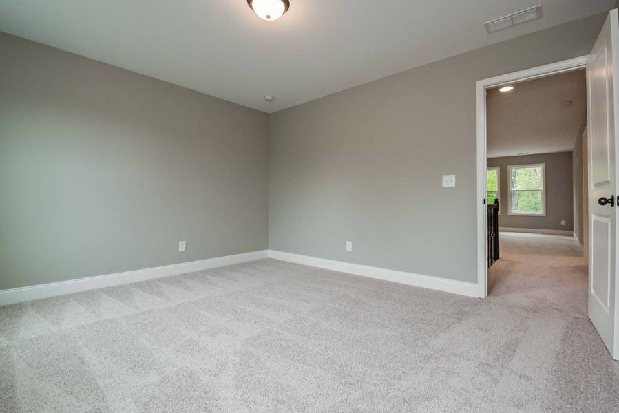 Empty bedroom with gray walls, white trim, and carpet, doorway to another room.