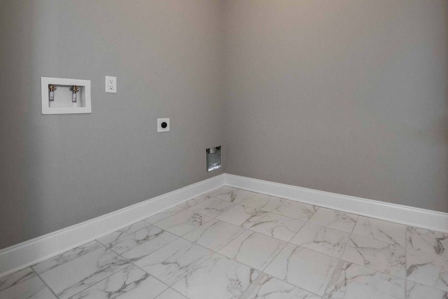 Empty laundry room with gray walls, white marble-look floor, and hookups for appliances.