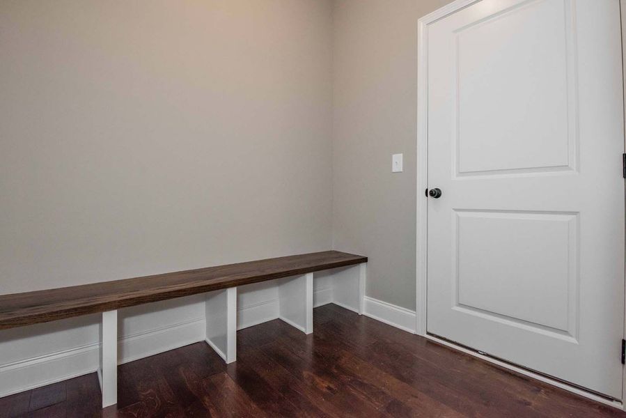 A mudroom with a wooden bench, white cubbies, dark wood floor, and a white door.