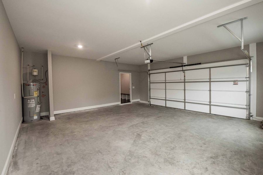 Empty garage with a water heater on the left and a closed white garage door on the right. Gray walls and floor.