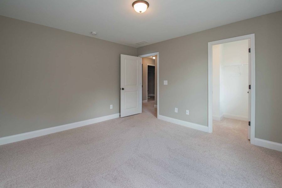 Empty bedroom with tan carpet, gray walls, and white trim. Two open doors lead to other rooms.