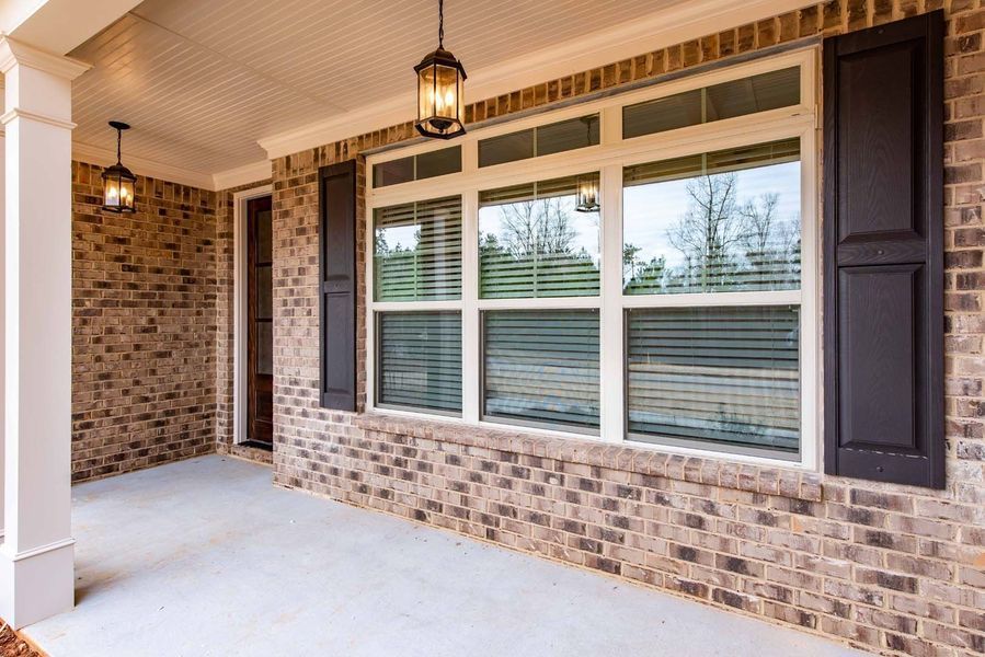 Porch with brick walls, large windows, dark shutters, and hanging lights.