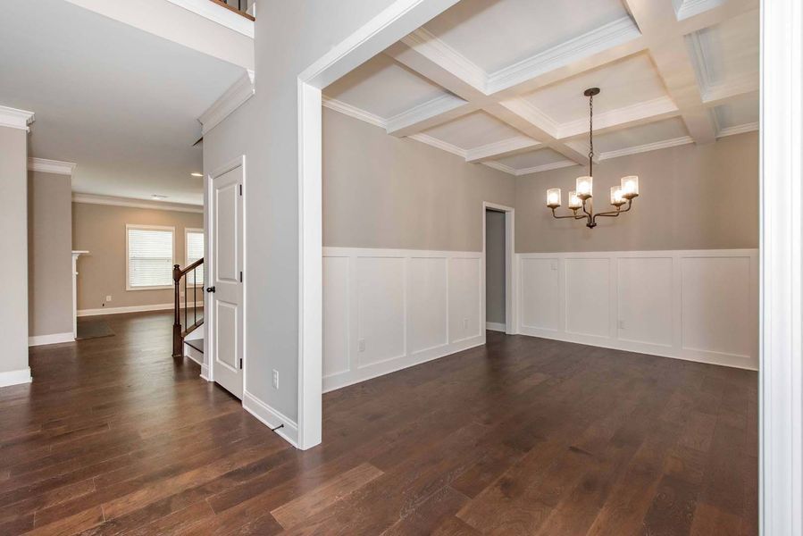 Spacious entryway with dark wood floors, leading to dining room with light-colored walls and a chandelier.
