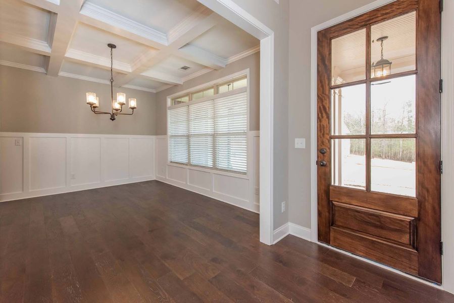 Empty dining room with dark wood floors, white wainscoting, and a glass-paneled wooden door.