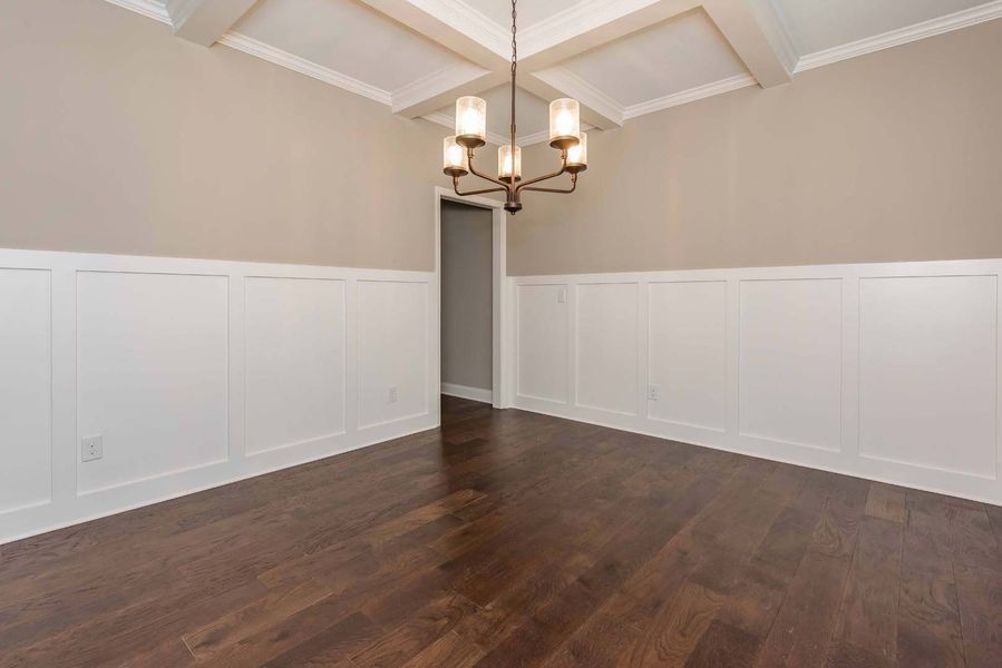 Empty dining room with dark hardwood floors, white paneling, beige walls, and a chandelier.