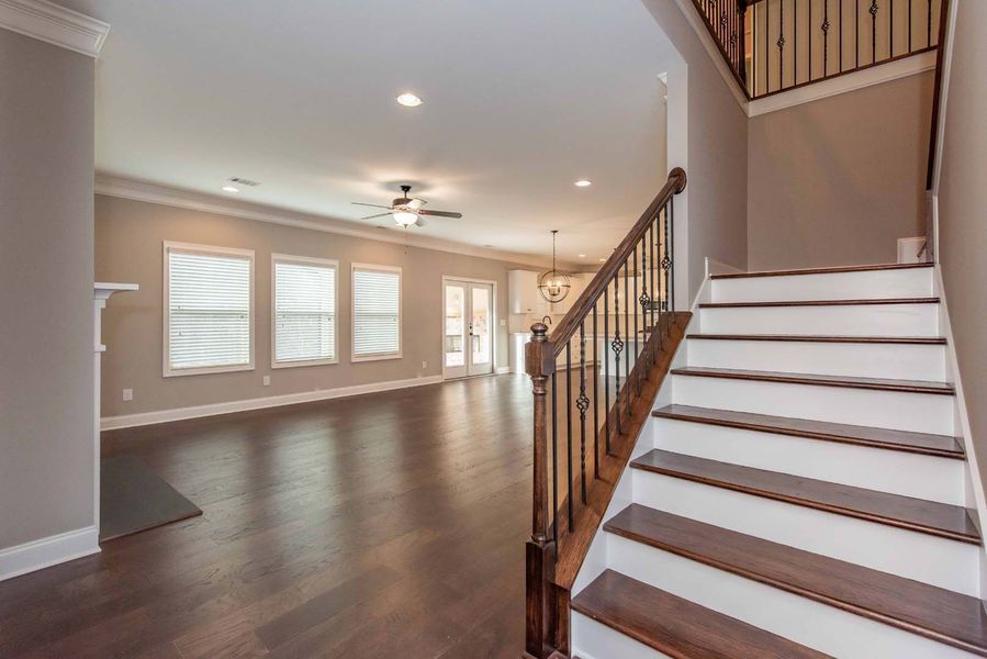 Interior view of a home with a staircase, hardwood floors, and a living room with windows.