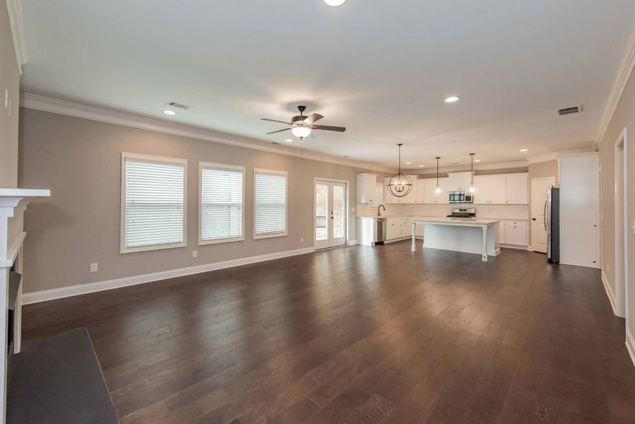 Open-concept living space with dark wood floors, kitchen, and windows with white trim.